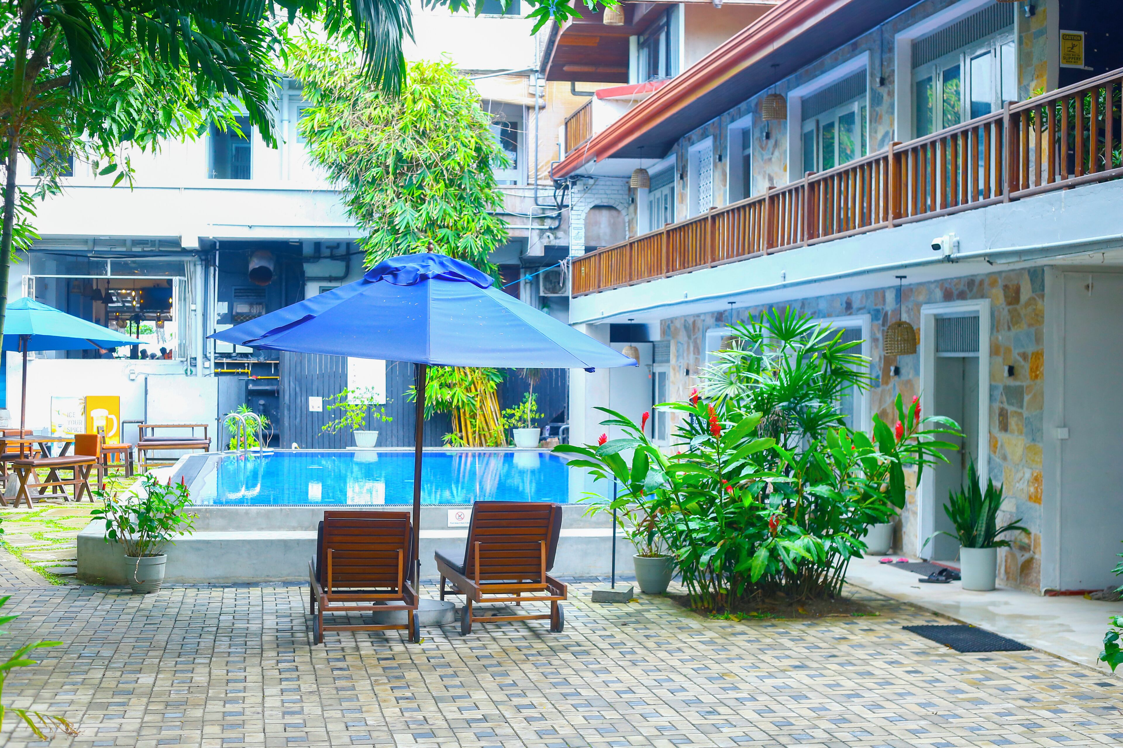 Un área de piscina con dos sillas de madera, una sombrilla azul y plantas en macetas.