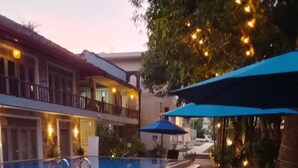 An outdoor pool area with stone tiles, wooden benches, and umbrellas.