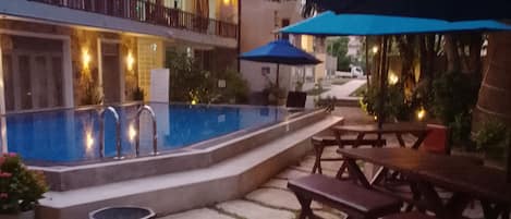 An outdoor pool area with stone tiles, wooden benches, and umbrellas.
