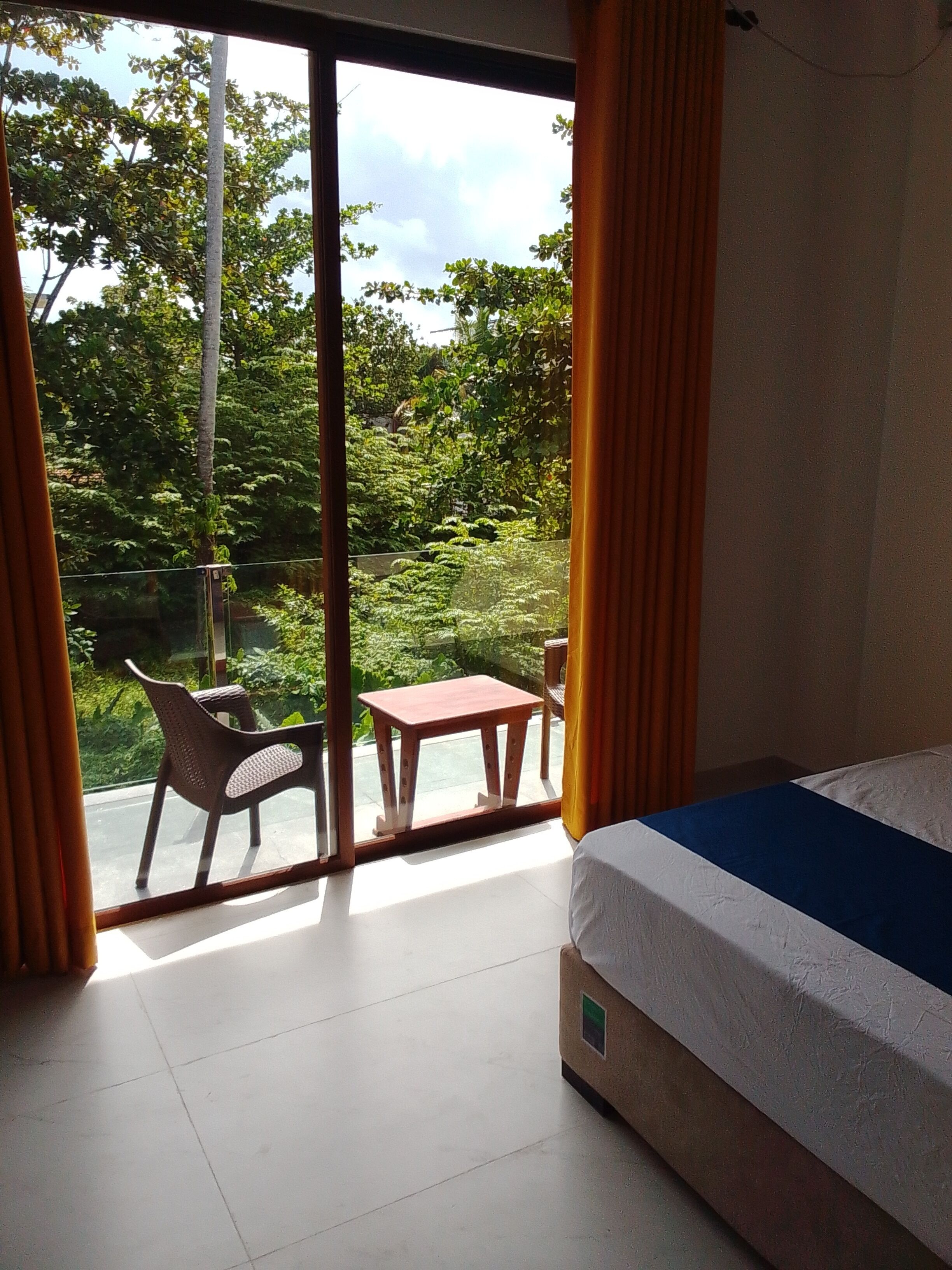 A room with a bed, a small table, and a chair, with a view of greenery outside.