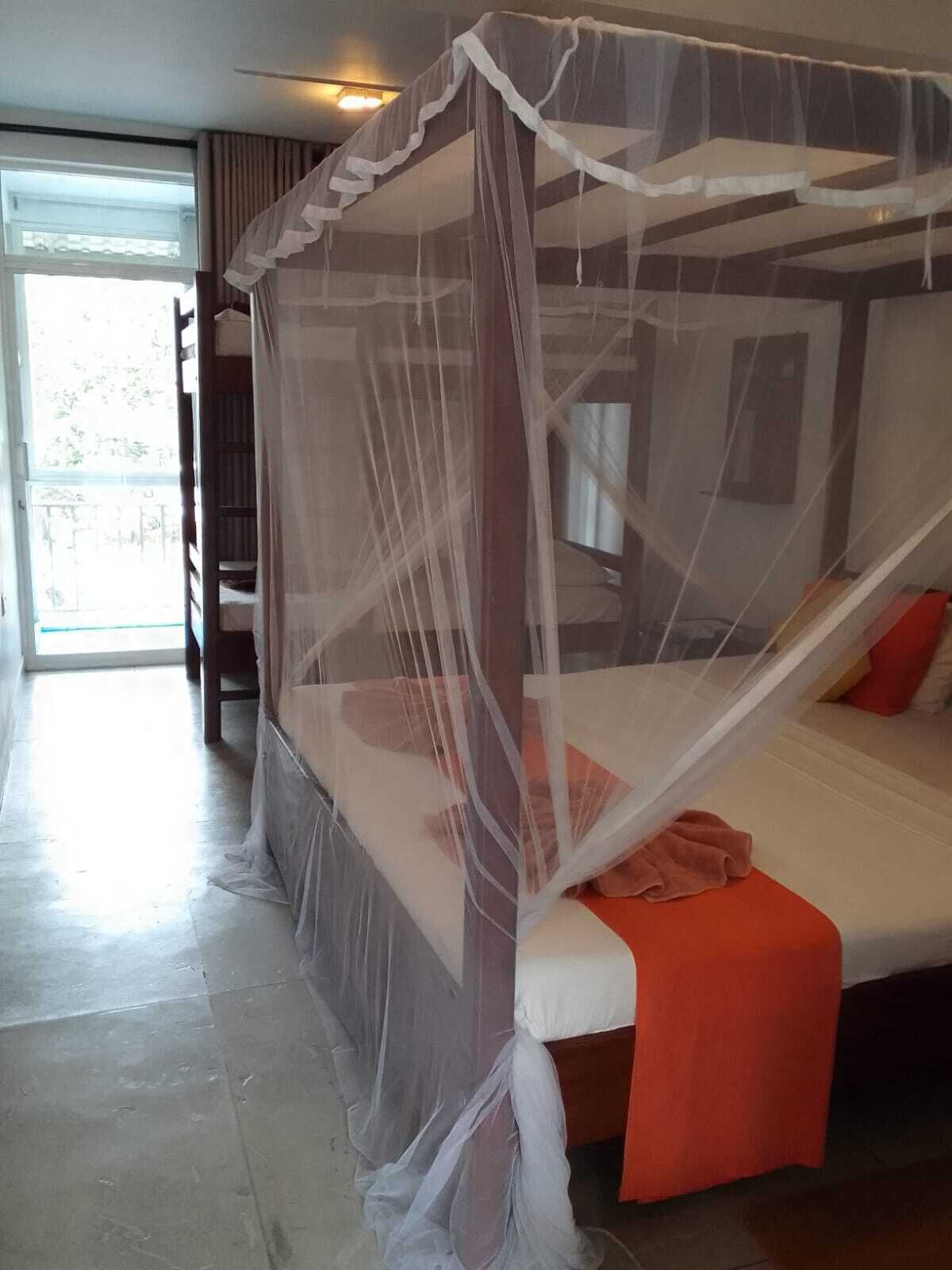 A room with a four-poster bed, a sliding glass door leading to a balcony, and a ceiling fan.