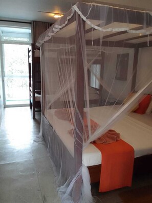 A room with a four-poster bed, a sliding glass door leading to a balcony, and a ceiling fan. - Seals Harbour Hotel (Weligama)
