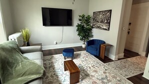 Uma sala de estar com ventilador de teto, televisão de tela plana, sofá, mesa de centro e tapete estampado.