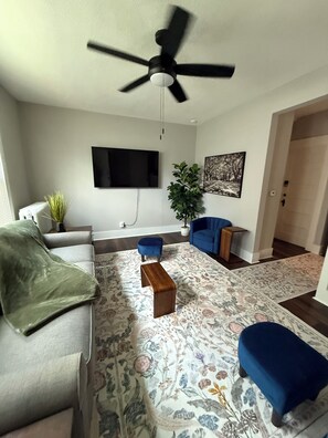 A living room with a ceiling fan, a flat-screen TV, a sofa, a coffee table, and a patterned rug. - Spacious Davenport 3BR/2BA Near Palmer College (Davenport)