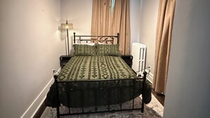 Quarto com cama, ventoinha no teto, radiador e janela com cortinas.