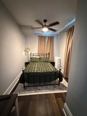 A bedroom with a bed, a ceiling fan, a radiator, and a window with curtains. - Spacious Davenport 3BR/2BA Near Palmer College (Davenport)
