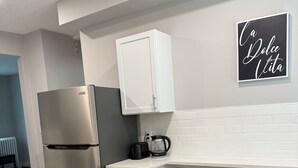 Uma cozinha compacta com geladeira de aço inoxidável, cafeteira e dois bancos.