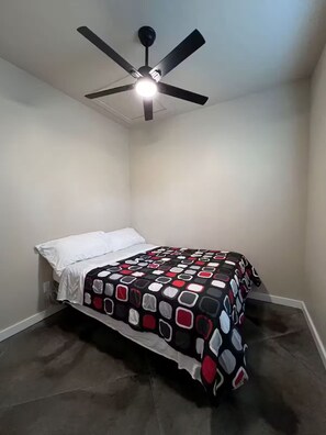 Ein Schlafzimmer mit einem Bett, einem Deckenventilator und einer gemusterten Bettdecke.