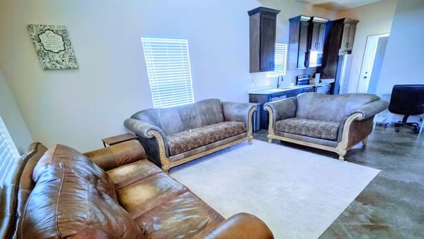 Una sala de estar con un sofá de cuero marrón, dos sillones, una mesa de centro y una cocina al fondo.