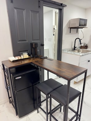 A compact kitchen with a built-in refrigerator, a coffee maker, and a microwave on a shelf.