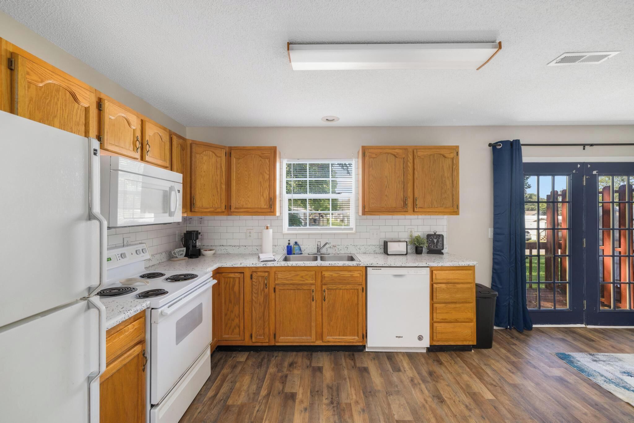 Una cocina con armarios de madera, un refrigerador blanco, un microondas, una estufa, un lavavajillas y una ventana con persianas.
