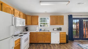 Una cocina con armarios de madera, un refrigerador blanco, un microondas, una estufa, un lavavajillas y una ventana con persianas.