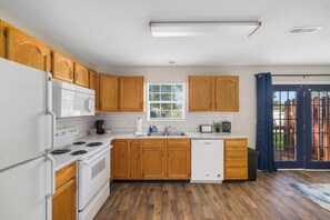 Una cocina con armarios de madera, un refrigerador blanco, un microondas, una estufa, un lavavajillas y una ventana con persianas.
