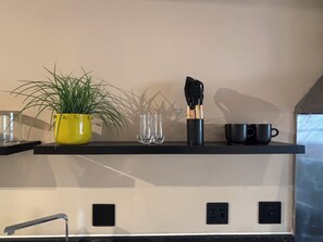 A kitchen shelf with a potted plant, glassware, and utensils. - Urban Escape | Mountain Views + Secure Parking (Cape Town)