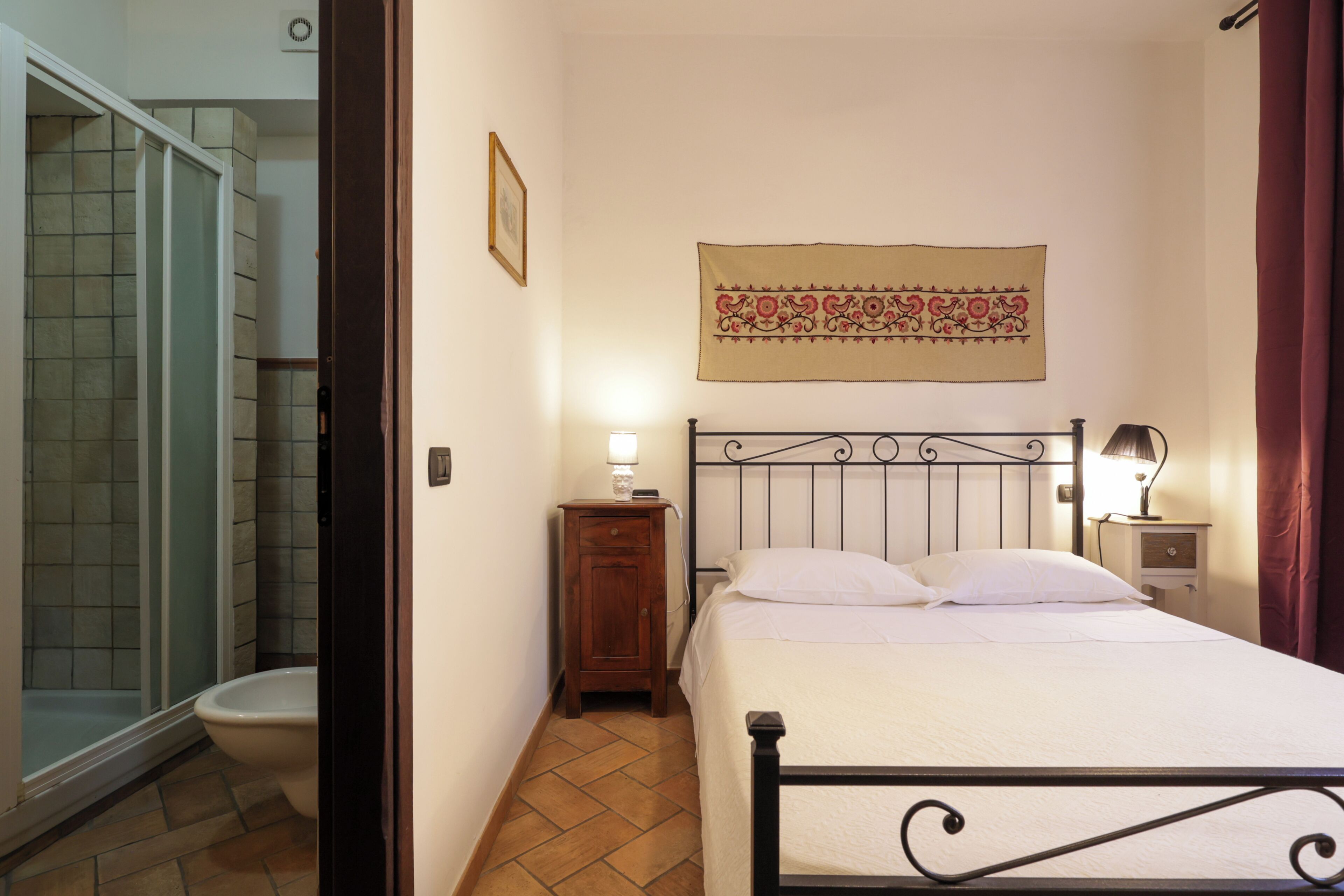 Ein Schlafzimmer mit einem Bett, einem Nachttisch mit Lampe, einer Wandteppich und einem Badezimmer mit Toilette und Dusche.