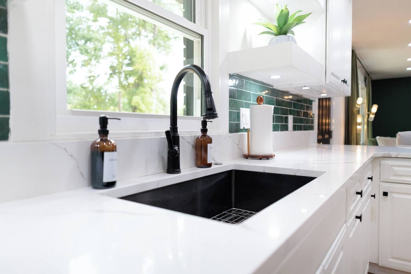 A modern kitchen with a large white countertop, a black faucet, and a window with a view of greenery.
