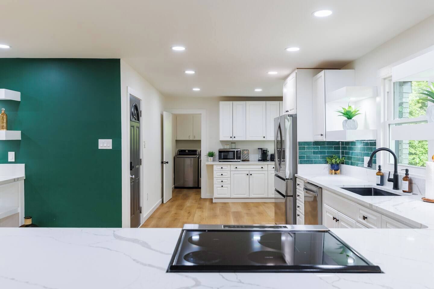 A modern kitchen with white cabinets, a stainless steel refrigerator, and a black induction cooktop.