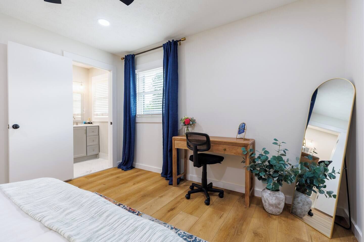 Una camera da letto con un letto, una scrivania con una sedia, uno specchio e una pianta in vaso.