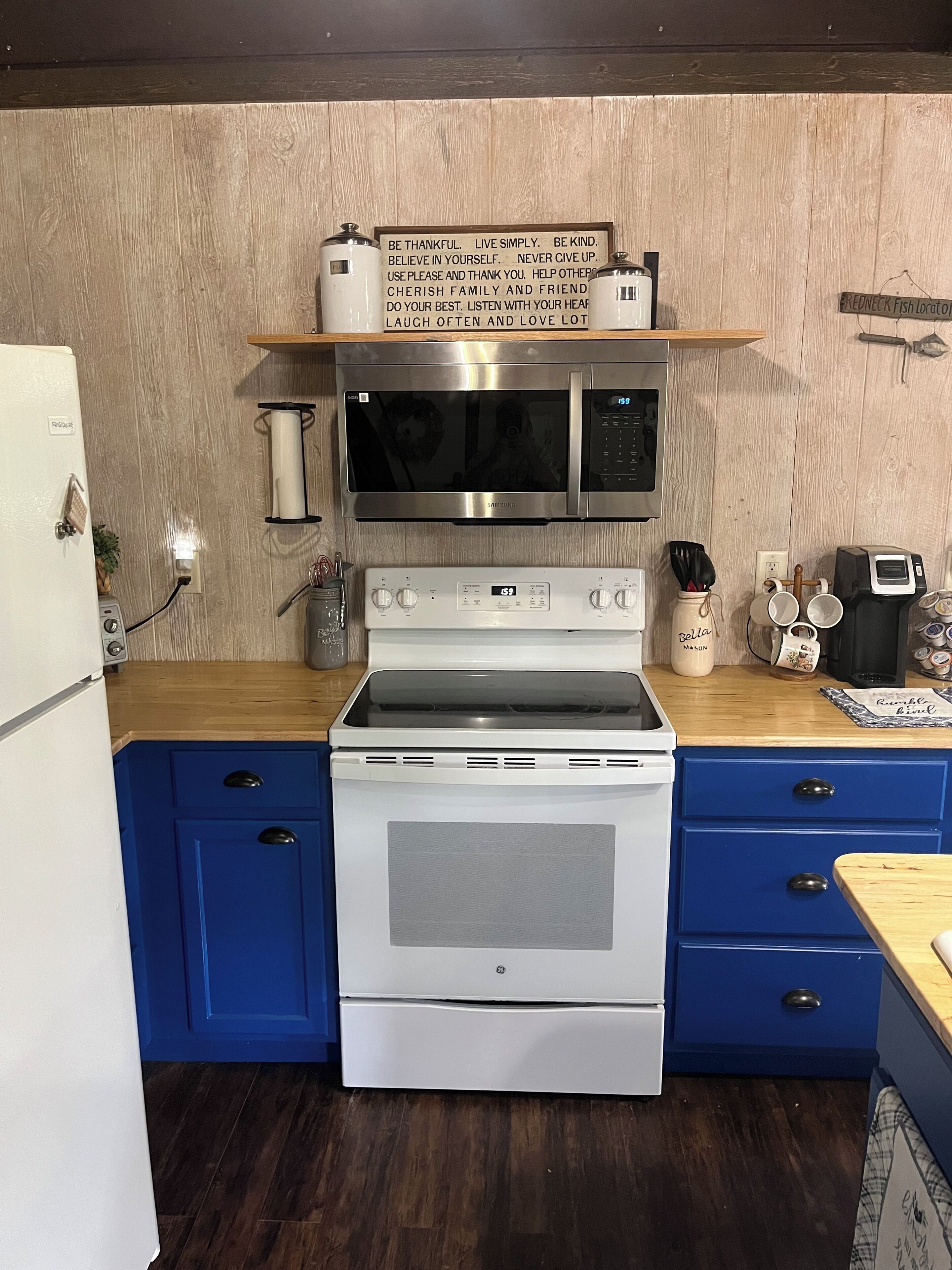 Una cocina con microondas de acero inoxidable, horno blanco, armarios azules y encimera de madera.