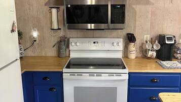 Una cocina con microondas de acero inoxidable, horno blanco, armarios azules y encimera de madera.