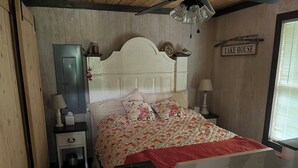 A bedroom with a wooden headboard, a bed with floral bedding, a nightstand with a lamp, and a sign reading 'LAKE HOUSE'. - Private Cabin on the lake with your own dock. (Decatur)