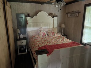 Ein Schlafzimmer mit einem hölzernen Kopfende, einem Bett mit floraler Bettwäsche, einem Nachttisch mit Lampe und einem Schild mit der Aufschrift 'LAKE HOUSE'.