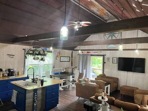 A spacious living area with a large TV, a dining area with a kitchen counter, and a ceiling fan.