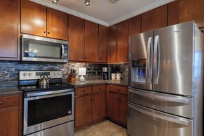 A kitchen with stainless steel appliances, wooden cabinets, a microwave, a refrigerator, and a coffee maker.