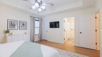 A bedroom with a bed, a ceiling fan, a TV, a dresser, and a door leading to another room.