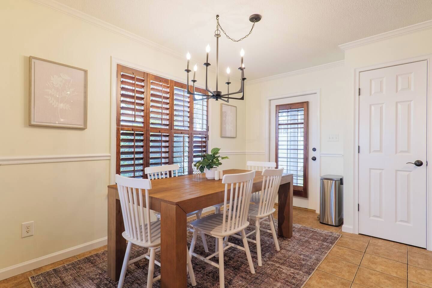 Un comedor con una mesa de madera y sillas blancas, una araña y una planta en maceta.