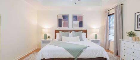 A bedroom with a bed, nightstands, a ceiling fan, and artwork on the wall.