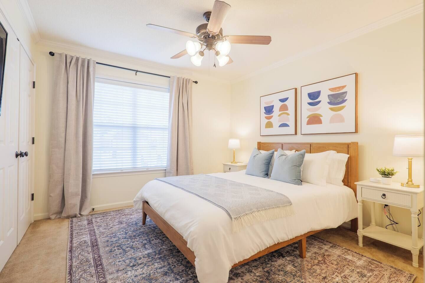 A bedroom with a bed, nightstands, a ceiling fan, a window with curtains, and wall art.