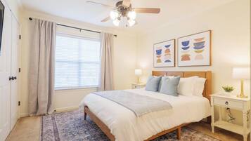 A bedroom with a bed, nightstands, a ceiling fan, a window with curtains, and wall art.