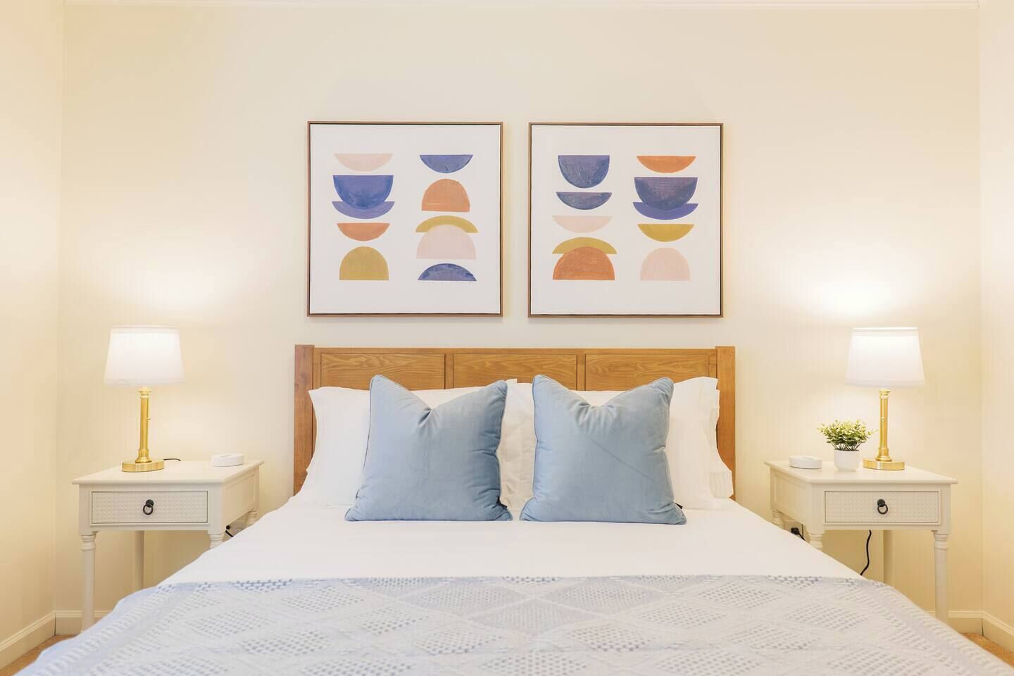 Habitación de hotel con cama, dos mesitas de noche, cabecera y dos cuadros abstractos enmarcados.