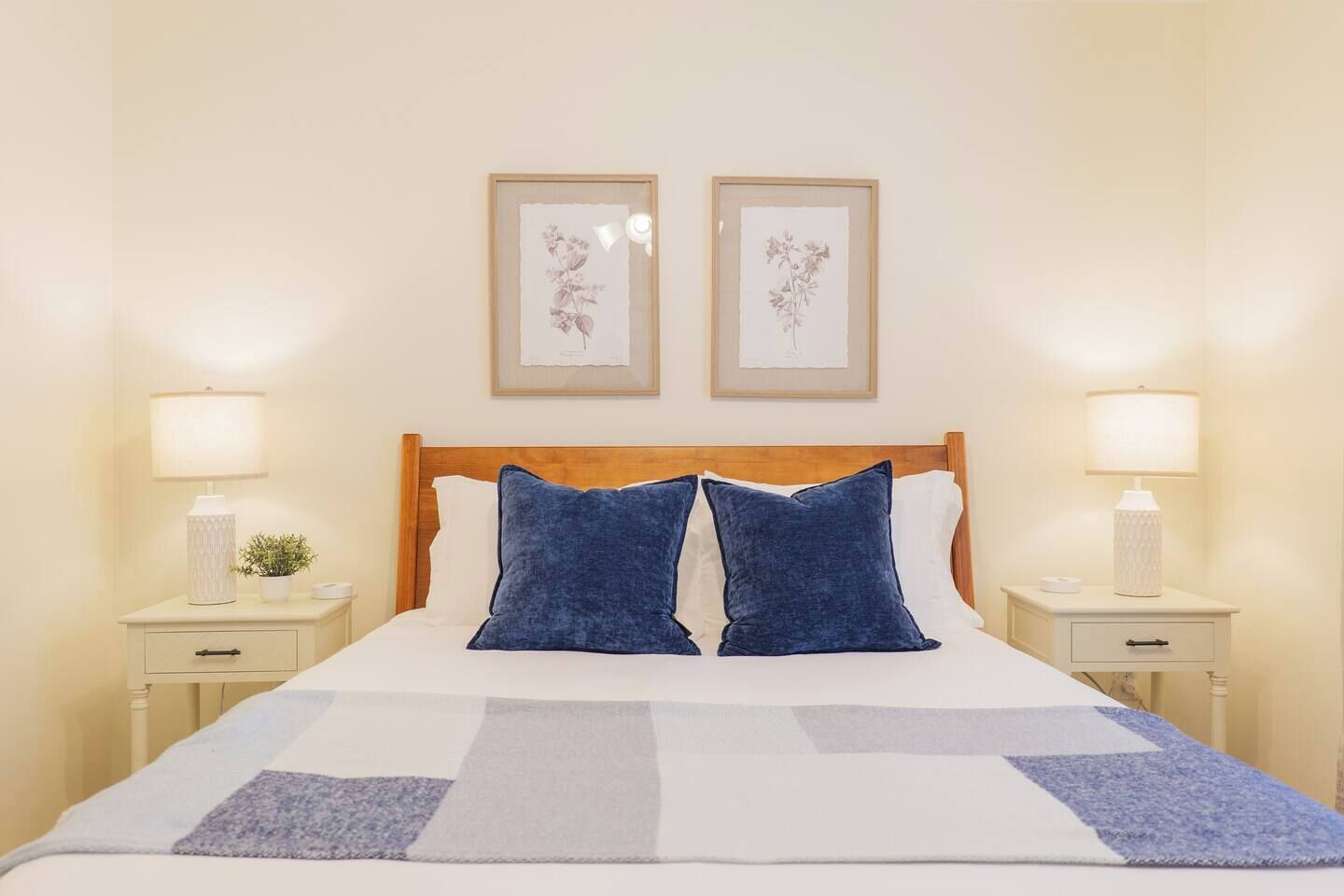 A bed with a wooden headboard, two pillows, a white blanket, and two bedside tables with lamps and a small plant.