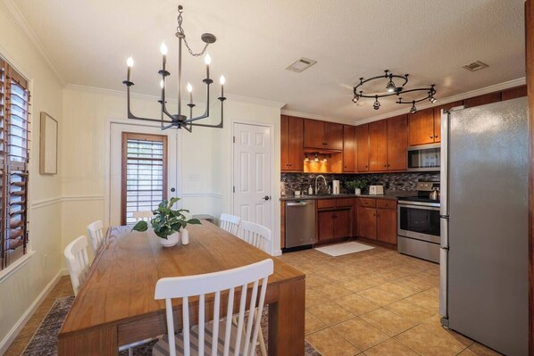 A modern kitchen with wooden cabinets, stainless steel appliances, and a dining area with a wooden table and chairs.