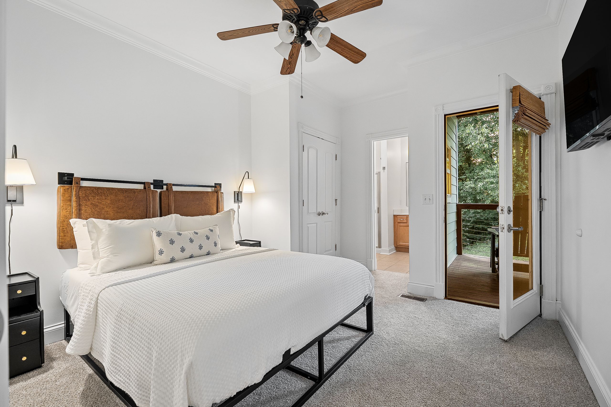 Une chambre à coucher avec un lit, des lampes de chevet, un ventilateur de plafond et une porte donnant sur un balcon.