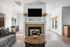 A living room with a fireplace, a television mounted above it, and a round coffee table with a cup.