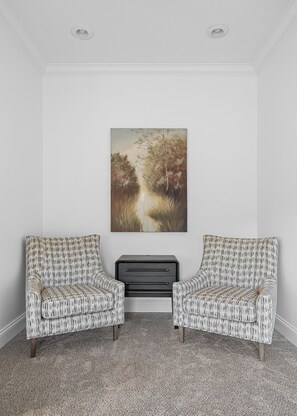 A room with two armchairs, a bench, and a painting on the wall.