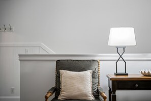A chair with a cushion, a lamp on a table, and a wall with a coat rack.