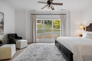 A bedroom with a large bed, a chair, a desk, and a window with curtains.