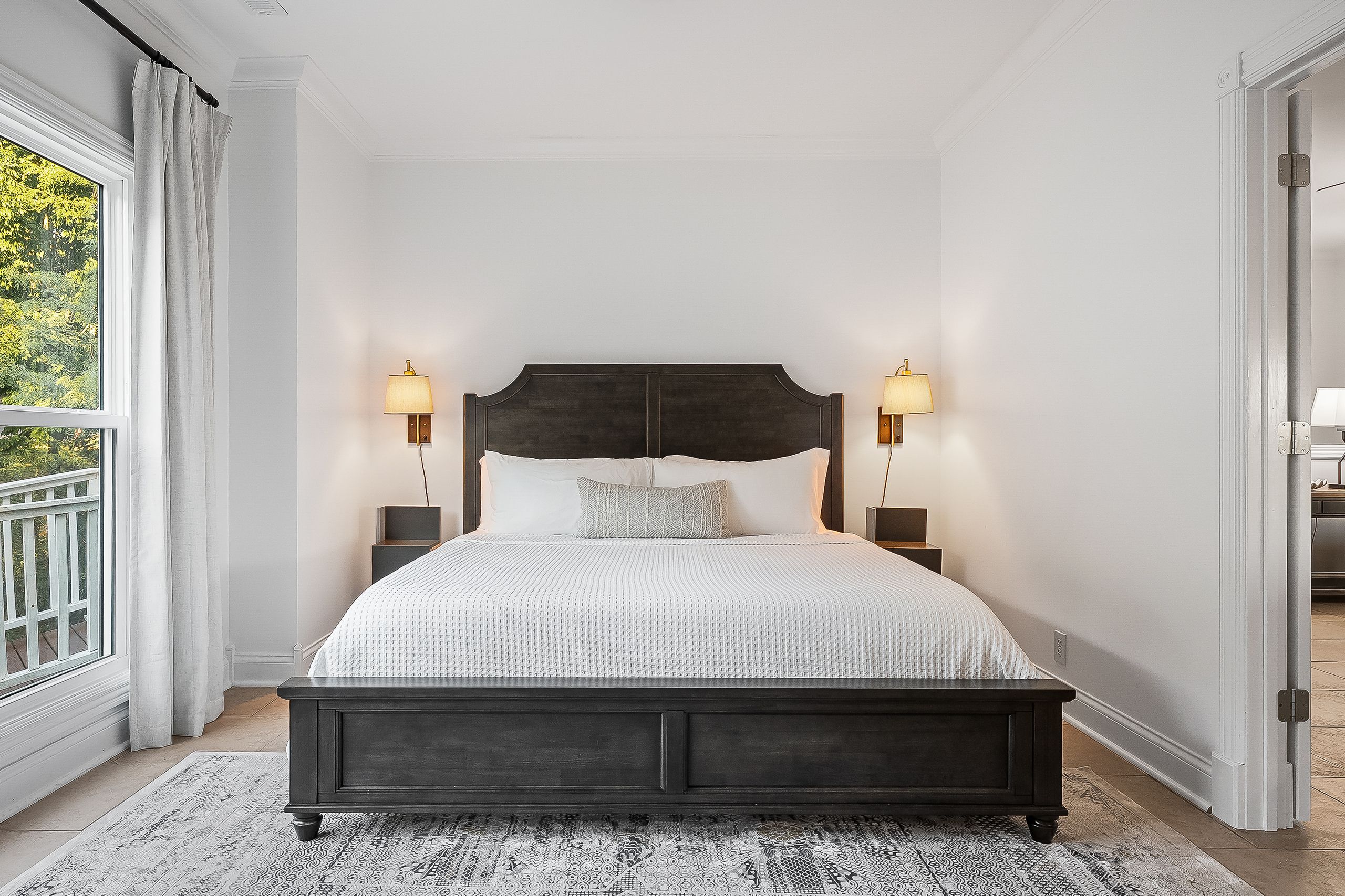 Ein Schlafzimmer mit einem großen Bett, zwei Nachttischlampen, einem dunklen Kopfteil und einem gemusterten Teppich.