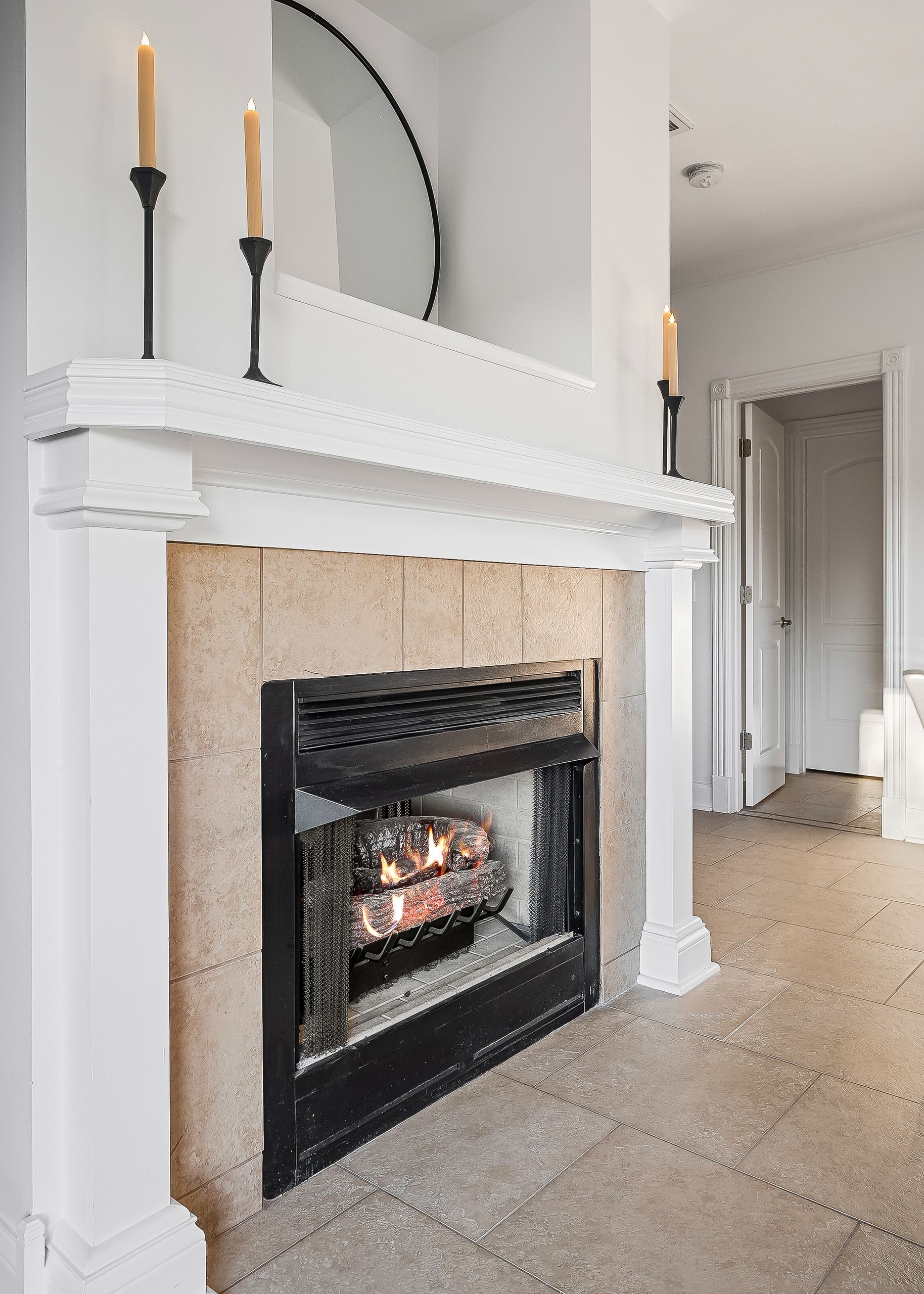 A fireplace with a white mantel, a mirror above it, and two candles.