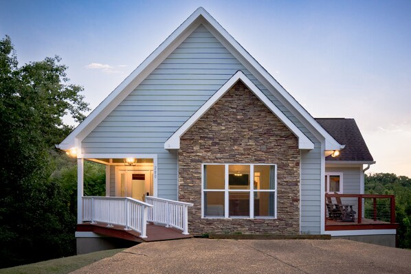 A residential house with a gabled roof, a stone facade, and a front porch with a white railing.