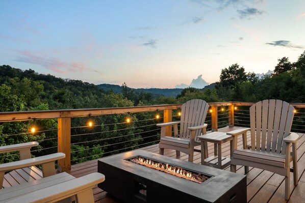 A deck with Adirondack chairs and a built-in fire feature, overlooking a forested landscape.