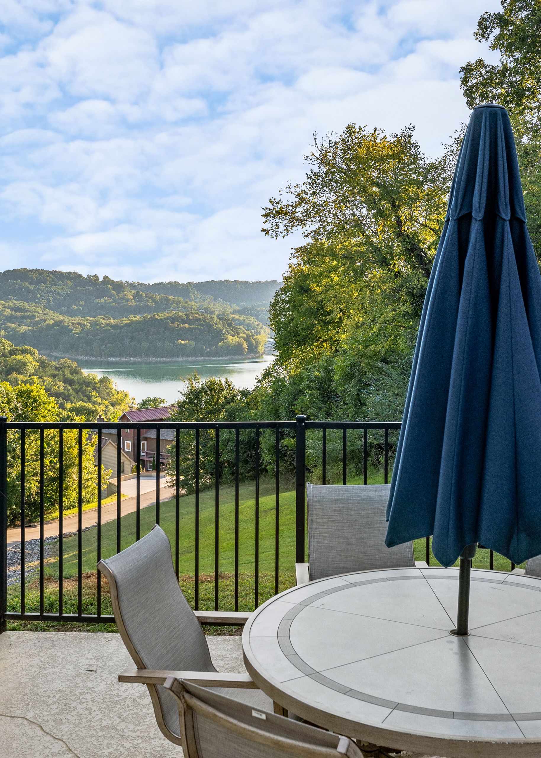 Ein Balkon mit rundem Tisch und Stühlen, mit Blick auf einen See und Hügel.