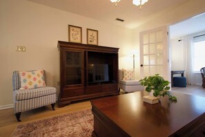 A living room with a wooden entertainment center, two upholstered chairs, a coffee table, and a potted plant. - Family-Friendly 4 Beds | Central & Fenced Yard (Valdosta)