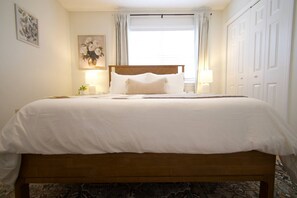 Een opgemaakt bed met een houten hoofdbord, wit beddengoed en twee bedlampjes.
