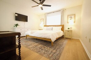 A bedroom with a bed, a ceiling fan, a TV mounted on the wall, and a bedside table with a lamp. - Family-Friendly 4 Beds | Central & Fenced Yard (Valdosta)
