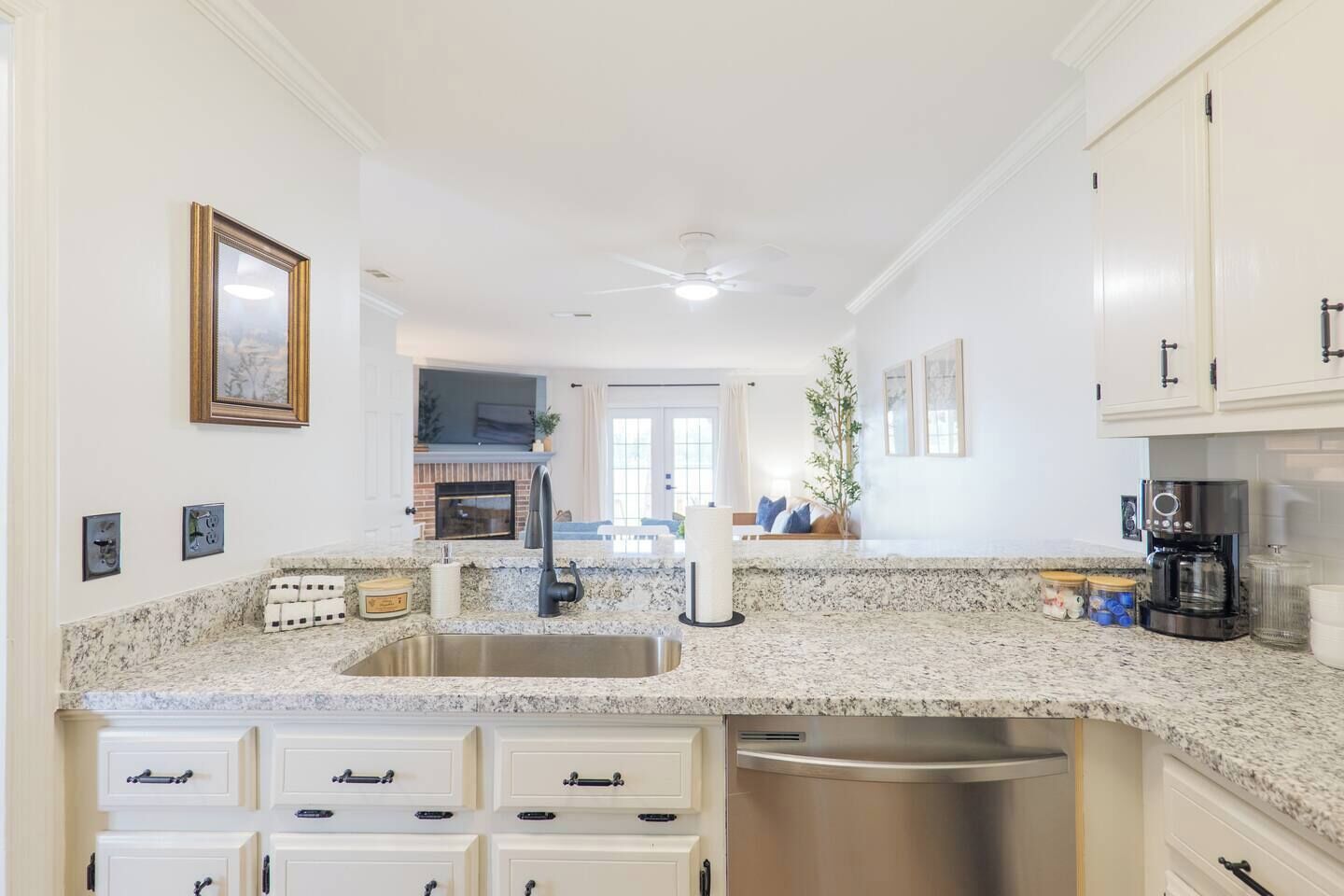 A kitchen with granite countertops, a stainless steel sink, white cabinetry, a built-in oven, and a ceiling fan.